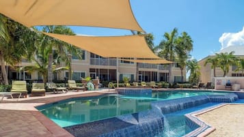 A pool area with lounge chairs, palm trees, and a building with balconies.