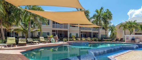 Un espace piscine avec des chaises longues, des palmiers et un bâtiment doté de balcons.