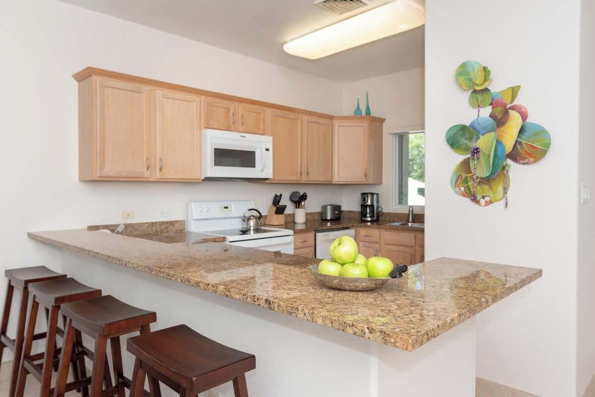 A modern kitchen with wooden cabinets, a granite countertop, and a fruit bowl.