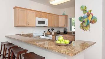 A modern kitchen with wooden cabinets, a granite countertop, and a fruit bowl.