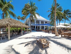 A beachside resort with thatched-roof structures, wooden benches, and palm trees.