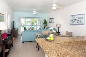 A modern living room with a blue sofa, a dining area with a granite table, and a kitchen area with a granite countertop.