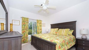 Ein Schlafzimmer mit Bett, Nachttisch, Kommode, Deckenventilator und Vorhängen.