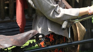 A person sitting on a wooden bench with a metal railing, wearing a headscarf and a grey top.