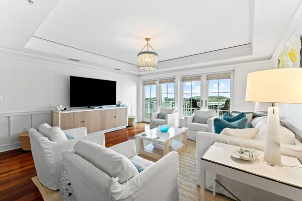 A spacious living room with a flat-screen TV, white sofas, a coffee table, and a chandelier. - Gulf and Pool Views with Beach Access (Santa Rosa Beach)