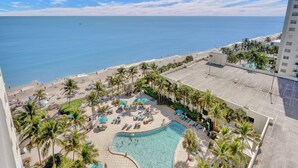 Un resort con piscina rodeada de palmeras y tumbonas, con vista a una playa y al océano.