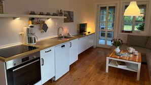 A modern kitchen with a Bosch oven, a coffee machine, and a sink. There is a dining area with a wooden table and a sofa. - Vacation home in the Elbtalaue to feel good all around (Dömitz OT Rüterberg)