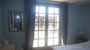 Ein Hotelzimmer mit Bett, Schreibtisch, Stuhl, Lampe, einem fenster mit Vorhängen und einem Spiegel.
