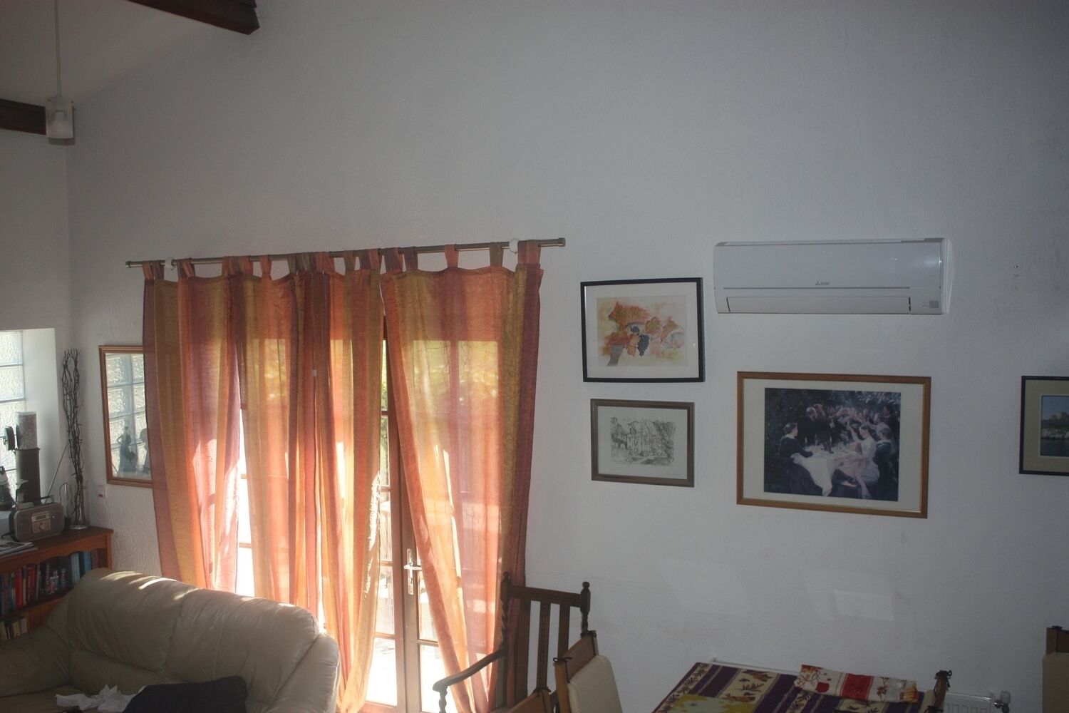 Una sala de estar con un sofá, una silla de madera, una estantería y una ventana con cortinas. Hay cuadros enmarcados en la pared.
