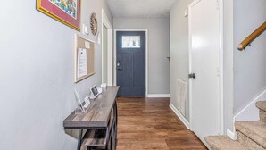 Un couloir avec un banc en bois, un tableau encadré, une porte avec une fenêtre et un escalier.