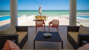 Ein überdachter Außenbereich mit Korbmöbeln, einem Tisch und Stühlen mit Blick auf Pool und Strand.