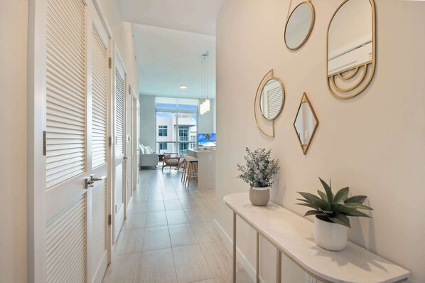 A hallway with a dining area in the background, a console table with a potted plant, and wall-mounted mirrors. - Stylish 1Bdrm Penthouse In Miami Design District (Miami)
