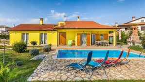 Une villa jaune avec une piscine et une terrasse en pierre.