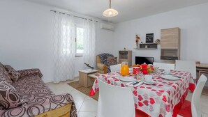 Un espacio habitable compacto con sofá, una mesa de comedor para dos personas, televisor y kitchenette.
