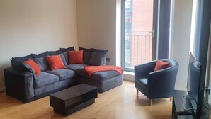 A modern living room with a sectional sofa, a coffee table, a TV, and a chair. - Manchester City Centre Apartment 1 Bed +sofa Bed (Manchester)