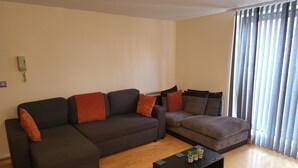 A living room with a sectional sofa, a smaller sofa, and a coffee table. - Manchester City Centre Apartment 1 Bed +sofa Bed (Manchester)