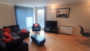 A living room with a sofa, a coffee table, a TV, and a radiator. - Manchester City Centre Apartment 1 Bed +sofa Bed (Manchester)