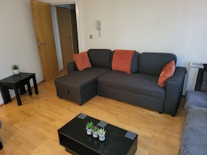 A modern living room with a sectional sofa, a small side table, a coffee table with plants, and a door leading to another room.