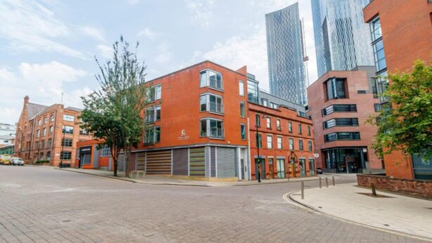 A modern urban street with red brick buildings, a paved road, and a sidewalk. - Manchester City Centre Apartment 1 Bed +sofa Bed (Manchester)