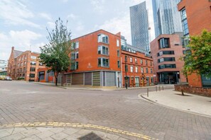 A modern urban street with red brick buildings, a paved road, and a sidewalk. - Manchester City Centre Apartment 1 Bed +sofa Bed (Manchester)