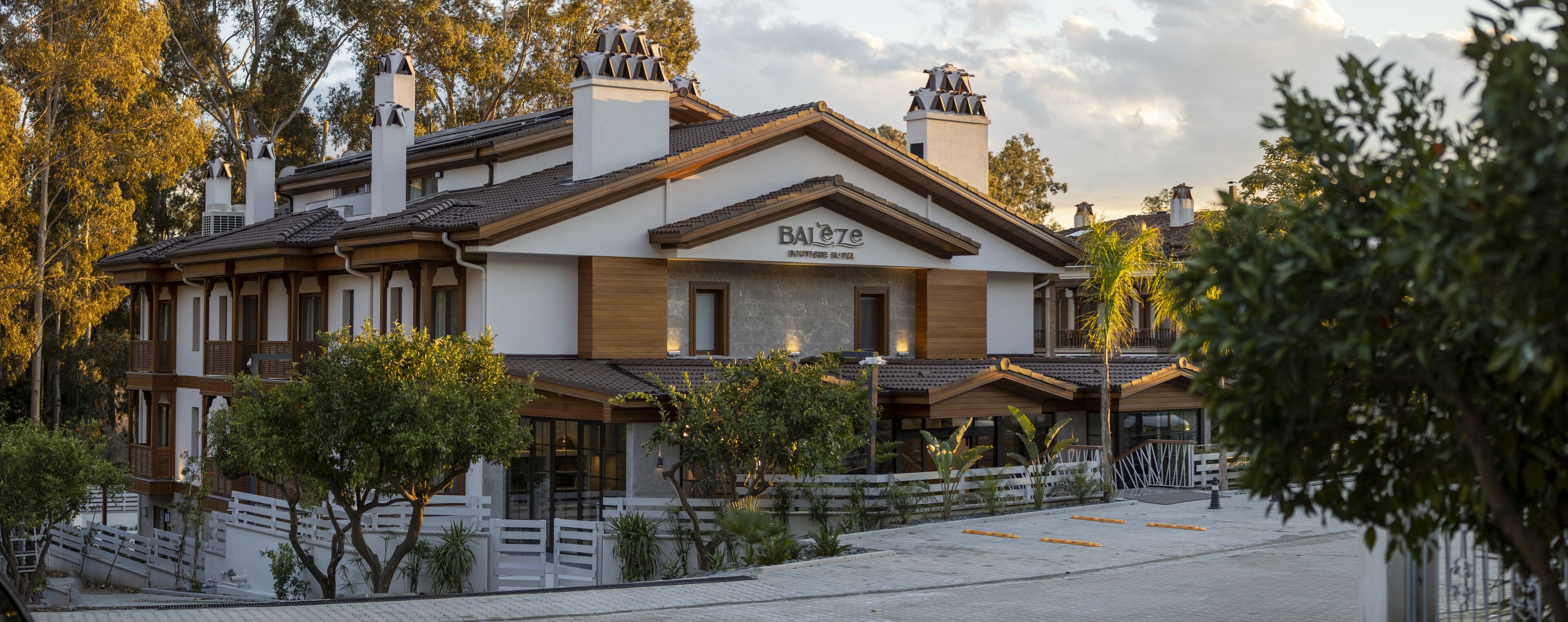 A hotel with a traditional architectural style, featuring a prominent signboard, multiple chimneys, and a well-maintained garden area.