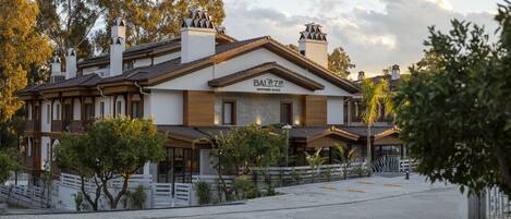 A hotel with a traditional architectural style, featuring a prominent signboard, multiple chimneys, and a well-maintained garden area.