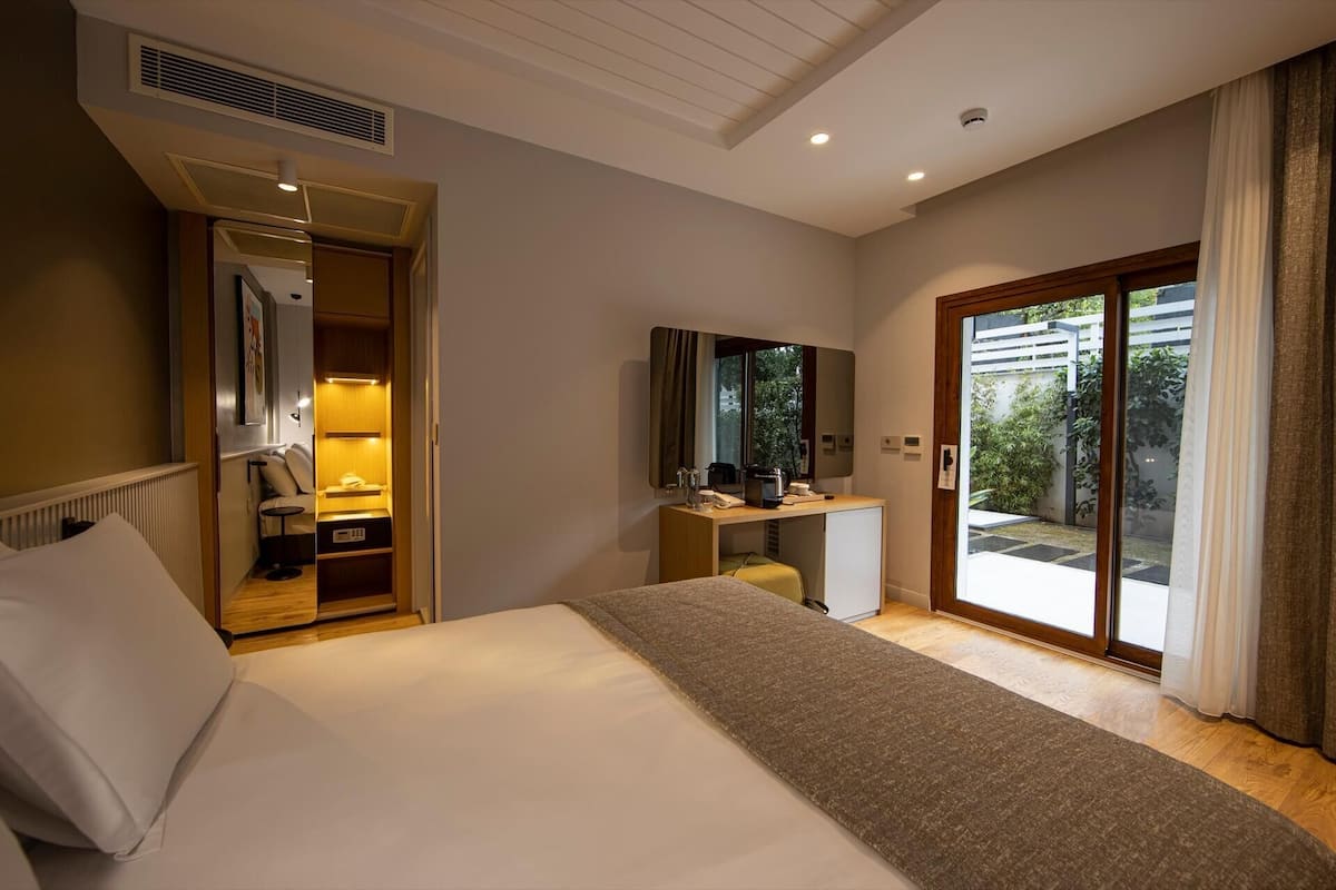 A hotel room with a bed, a desk with a computer, a mirror, and a sliding glass door to a balcony.