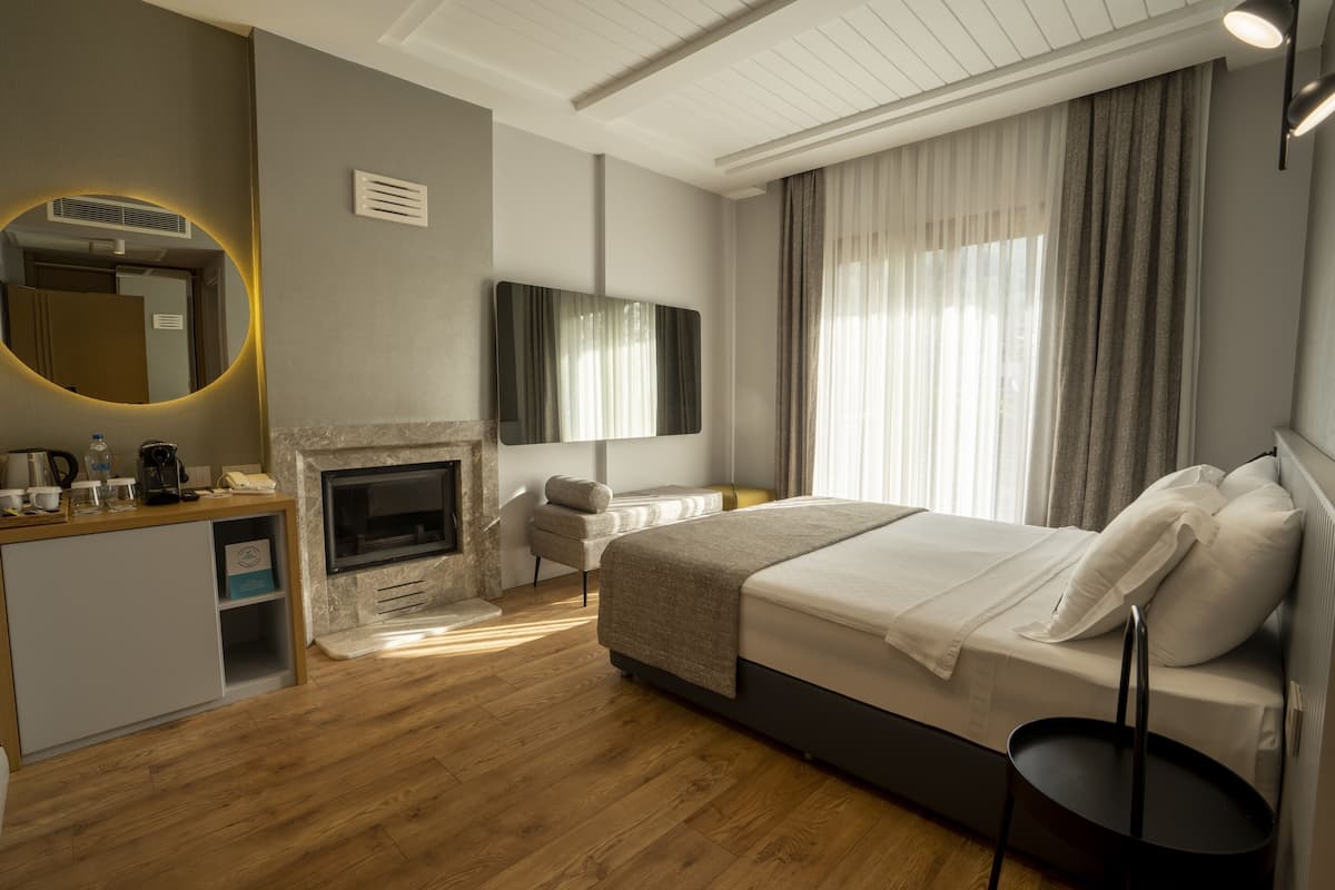 A modern hotel room with a fireplace, a bed, a desk, and a large mirror.