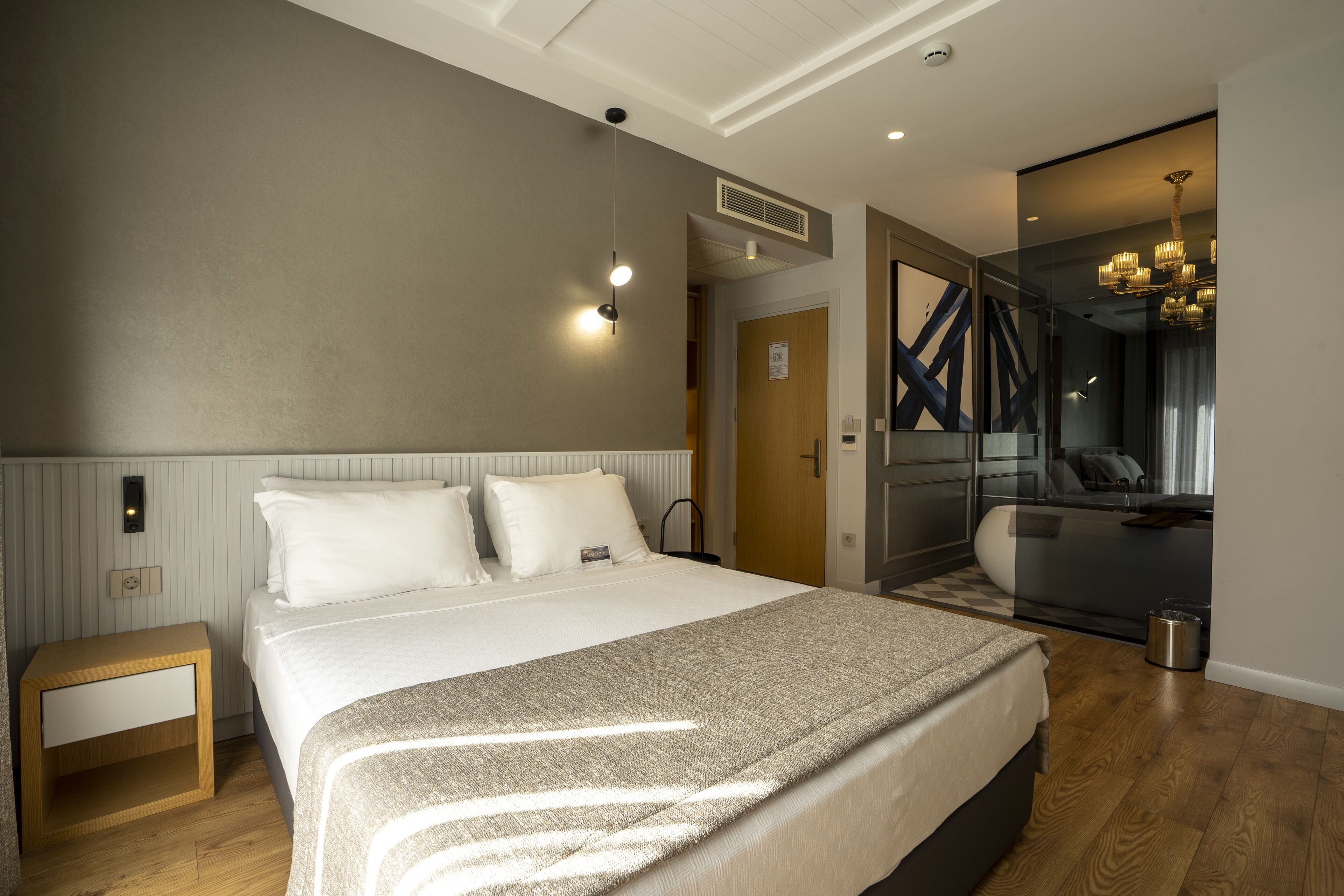 Una habitación de hotel moderna con una cama grande, una mesita de noche y un espejo con marco decorativo.