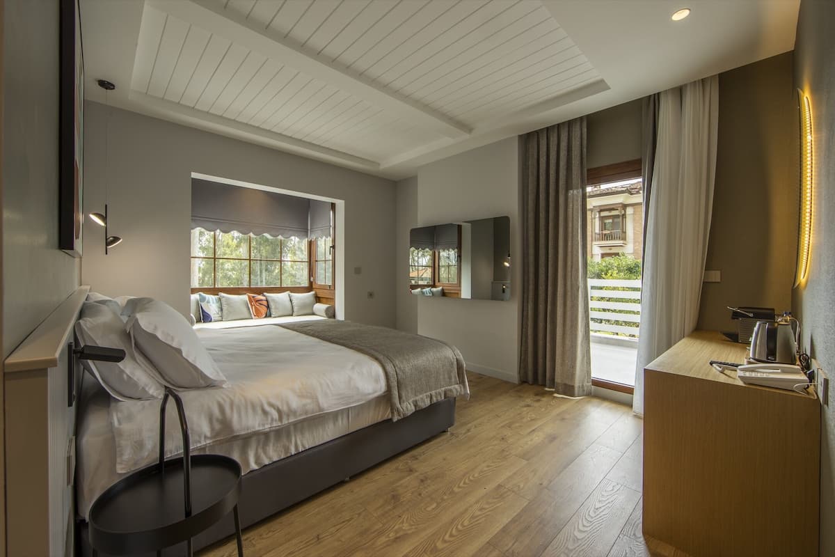 A modern bedroom with a large bed, a desk, and a view of the outdoors.