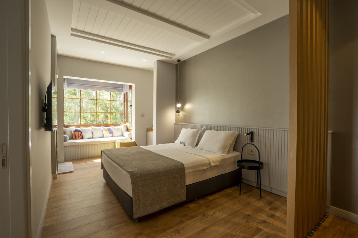 A bedroom with a bed, bedside table, lamp, window, and built-in bench.