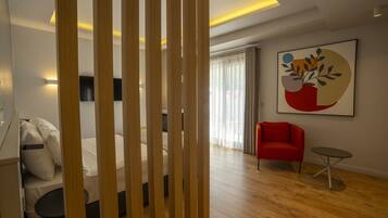 Una habitación de hotel moderna con una cama, un sillón rojo, una mesita y un televisor de pared.