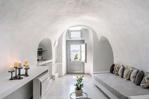 A narrow, white-walled interior with a kitchen area, a seating area with cushions, and a potted plant.