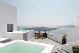 A modern outdoor terrace with a view of the sea, a small table with chairs, and a potted plant.