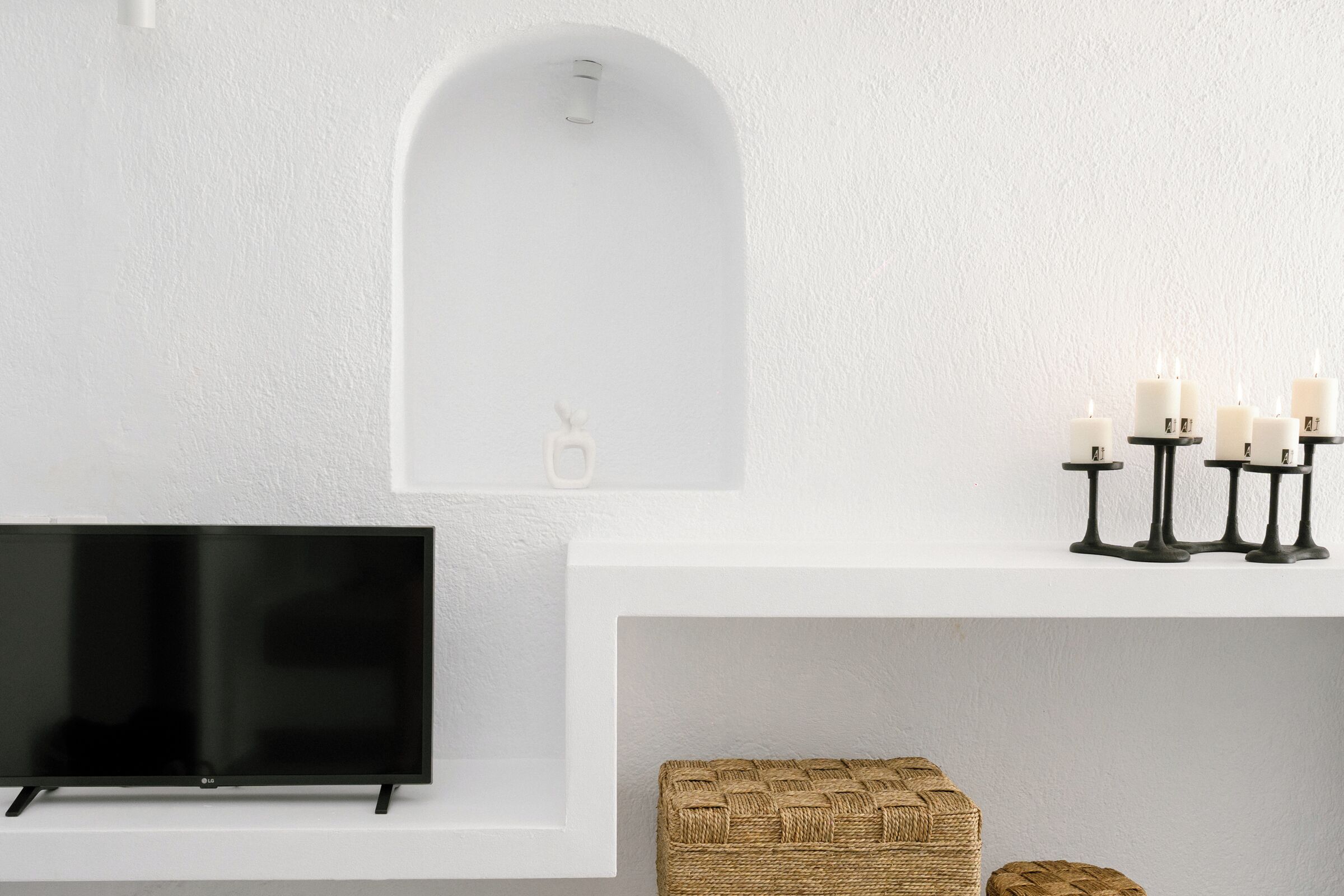 A modern living room with a flat-screen TV, a white fireplace, and a woven pouf.