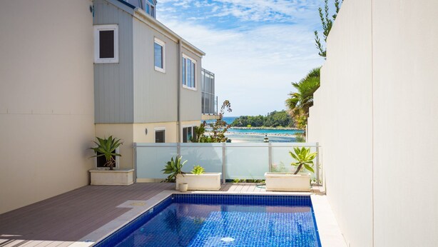 En swimmingpool med udsigt over havet, omgivet af en bygning med store vinduer og plantekasser.