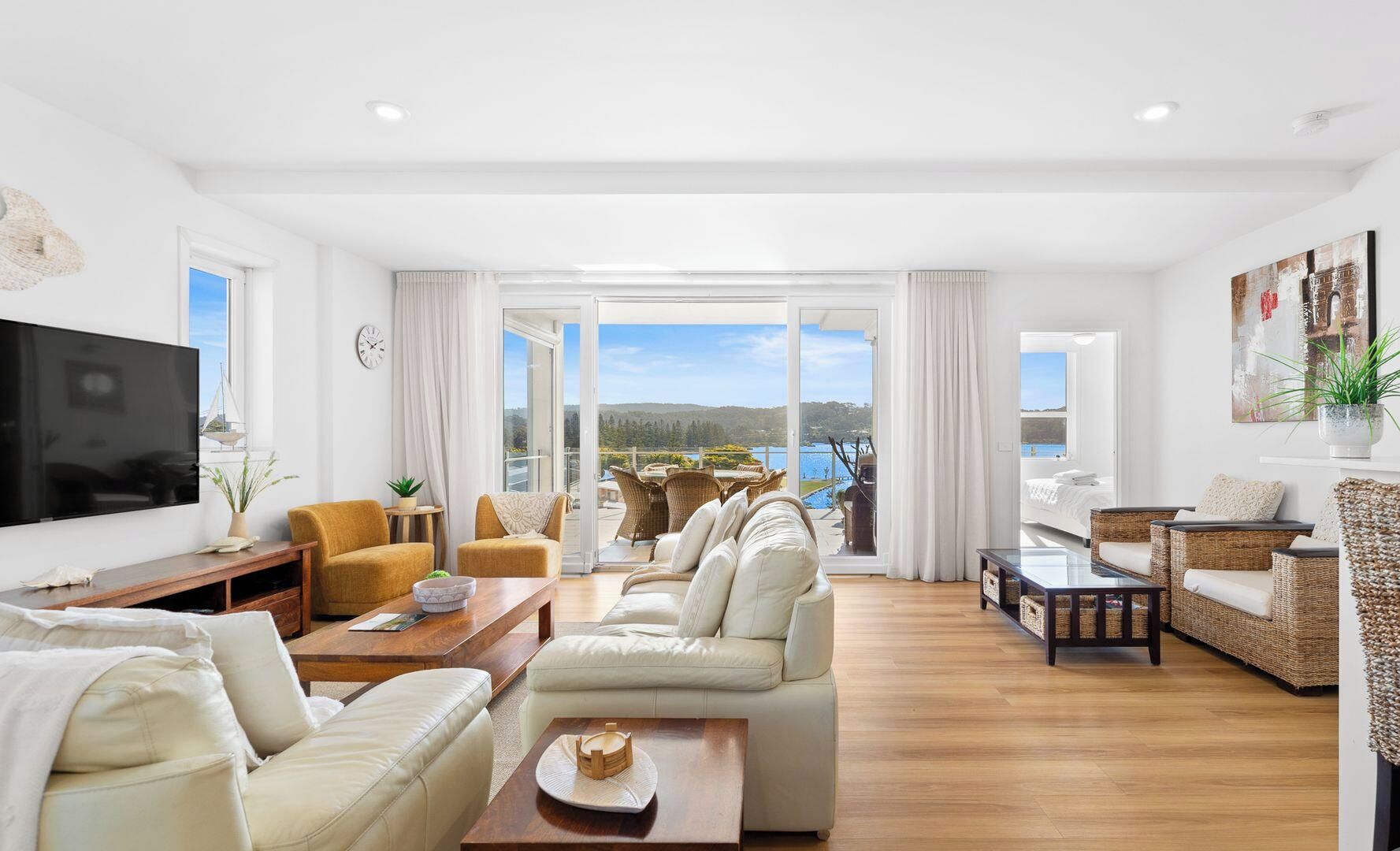A spacious living area with a large flat-screen TV, comfortable seating, and a balcony with a scenic view.