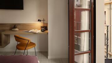 A modern room with a wooden desk, an orange chair, a small plant, and a window with a view of buildings.