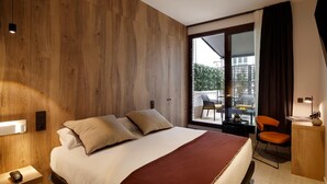 Ein modernes Hotelzimmer mit einem großen Bett, einem Schreibtisch und einem Sessel. Das Zimmer verfügt über eine Holzwand und ein großes Fenster mit Blick auf die Stadt.
