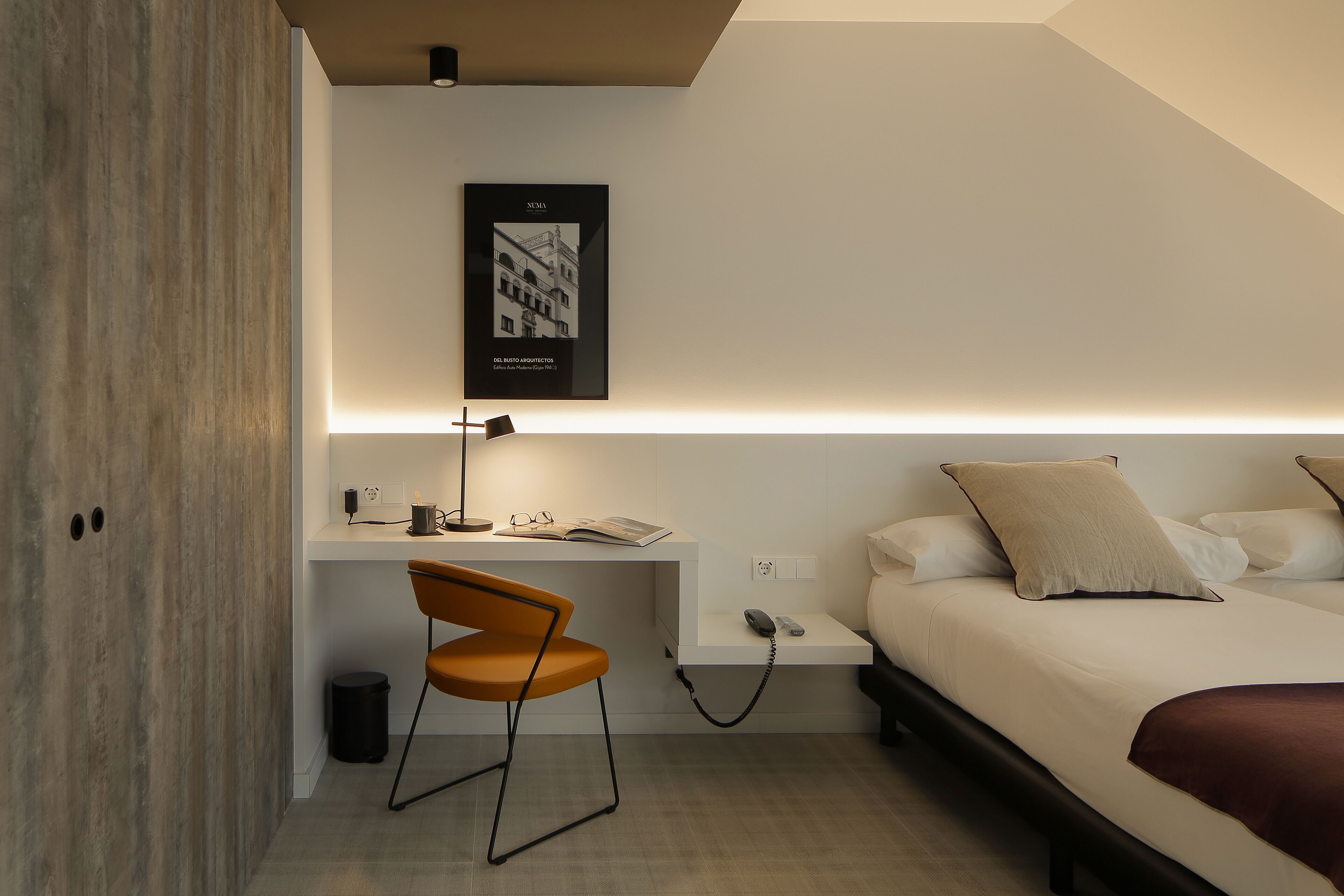 Ein modernes Hotelzimmer mit Schreibtisch, Stuhl und einem Bett mit Kopfteil.