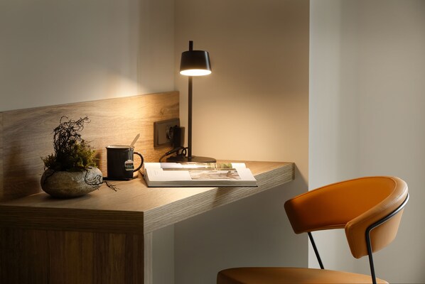 Un espacio de trabajo con un escritorio de madera, una lámpara, una taza, un libro y una silla.