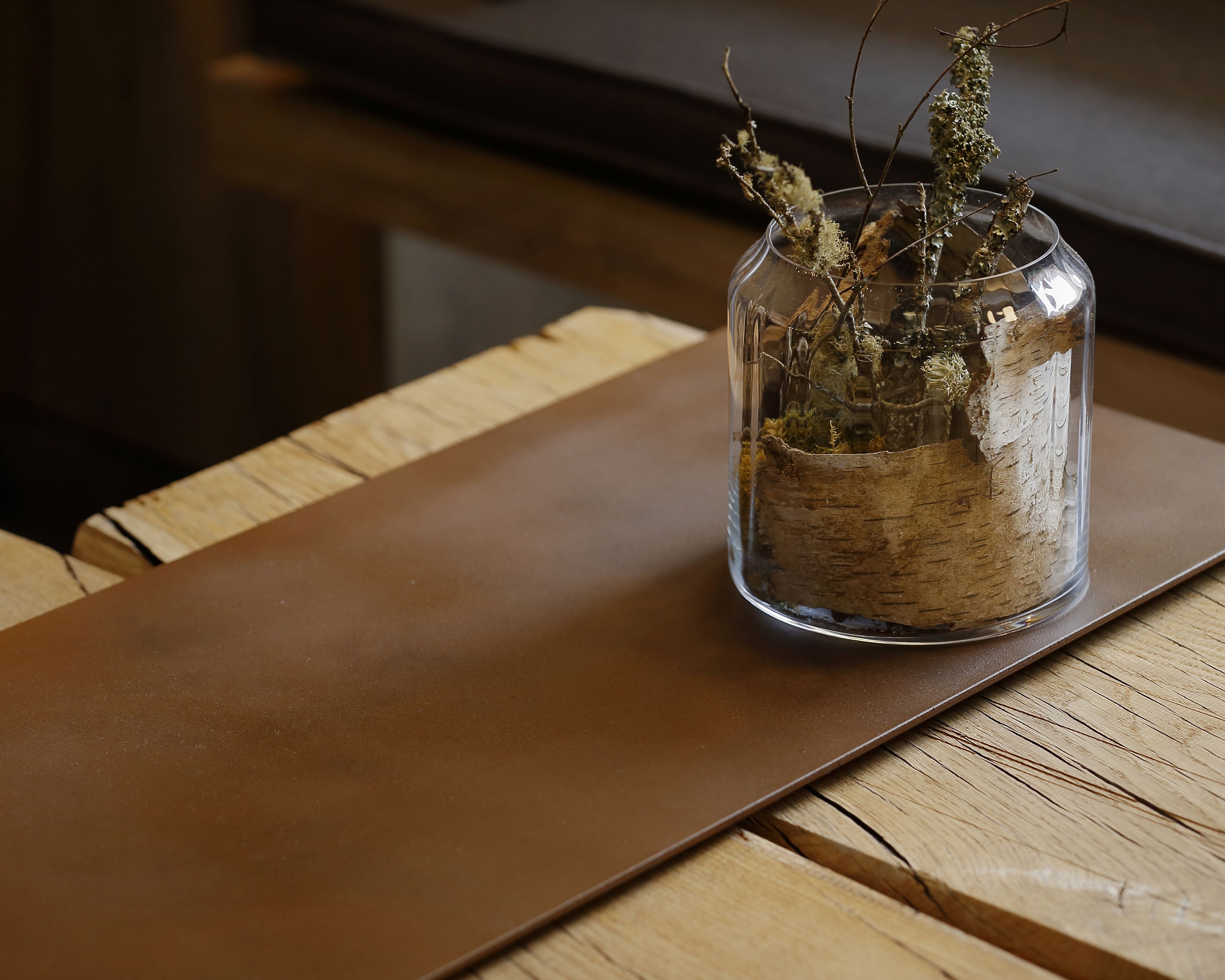 Un bocal en verre transparent contenant des plantes séchées, posé sur une table en bois.