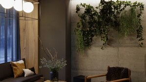 Ein gemütlicher Wohnbereich mit einer Couch, einem Holztisch und einem Sessel. Eine Vase mit Zweigen und eine Wandpflanze sind vorhanden.