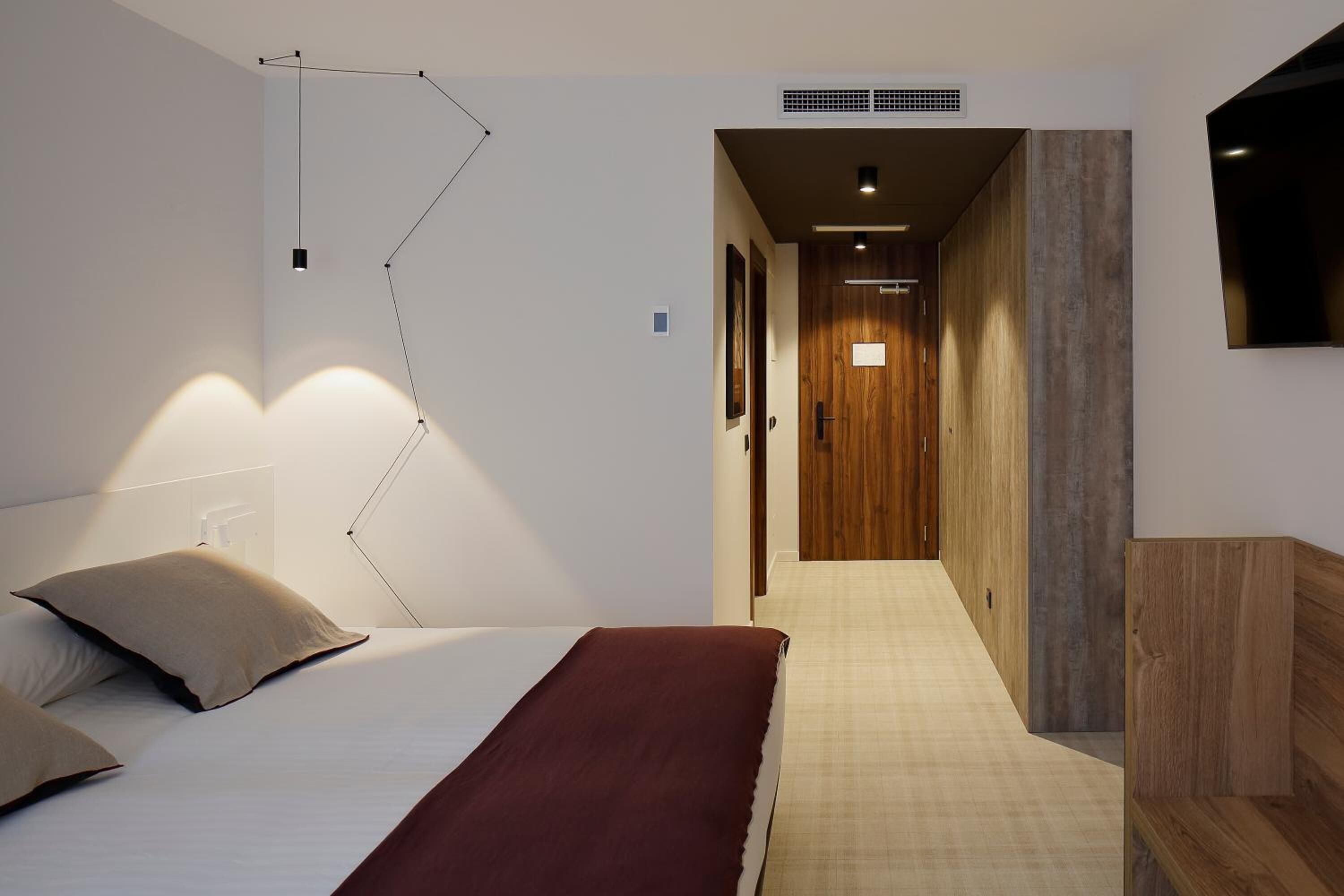 A bedroom with a bed, bedside table, and a wall-mounted TV.