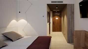 A bedroom with a bed, bedside table, and a wall-mounted TV.