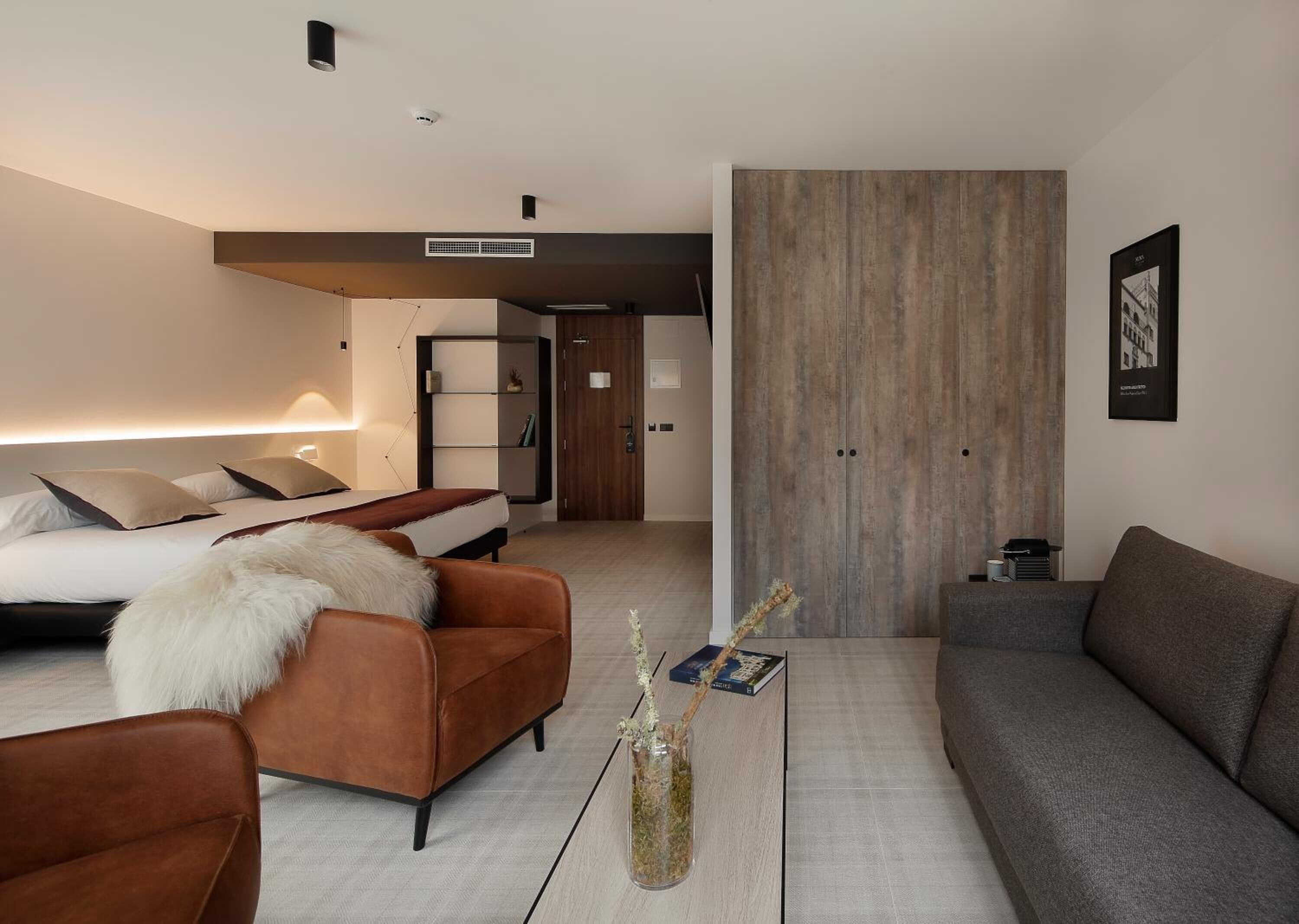 A modern hotel room with a bed, a sofa, a coffee table, and a large wooden panel wall.