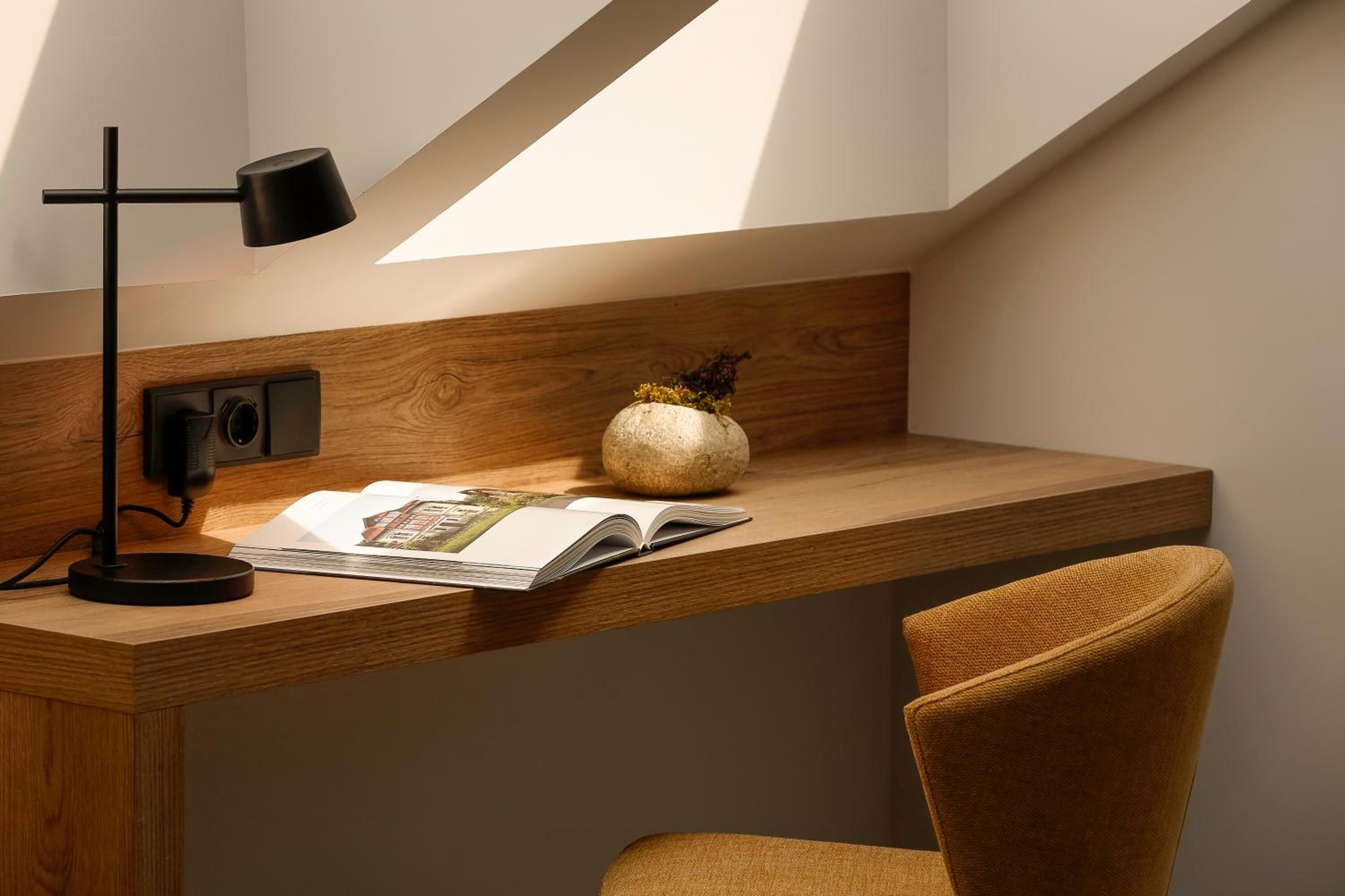 A wooden desk with a black desk lamp, a vase with dried flowers, and an open book.