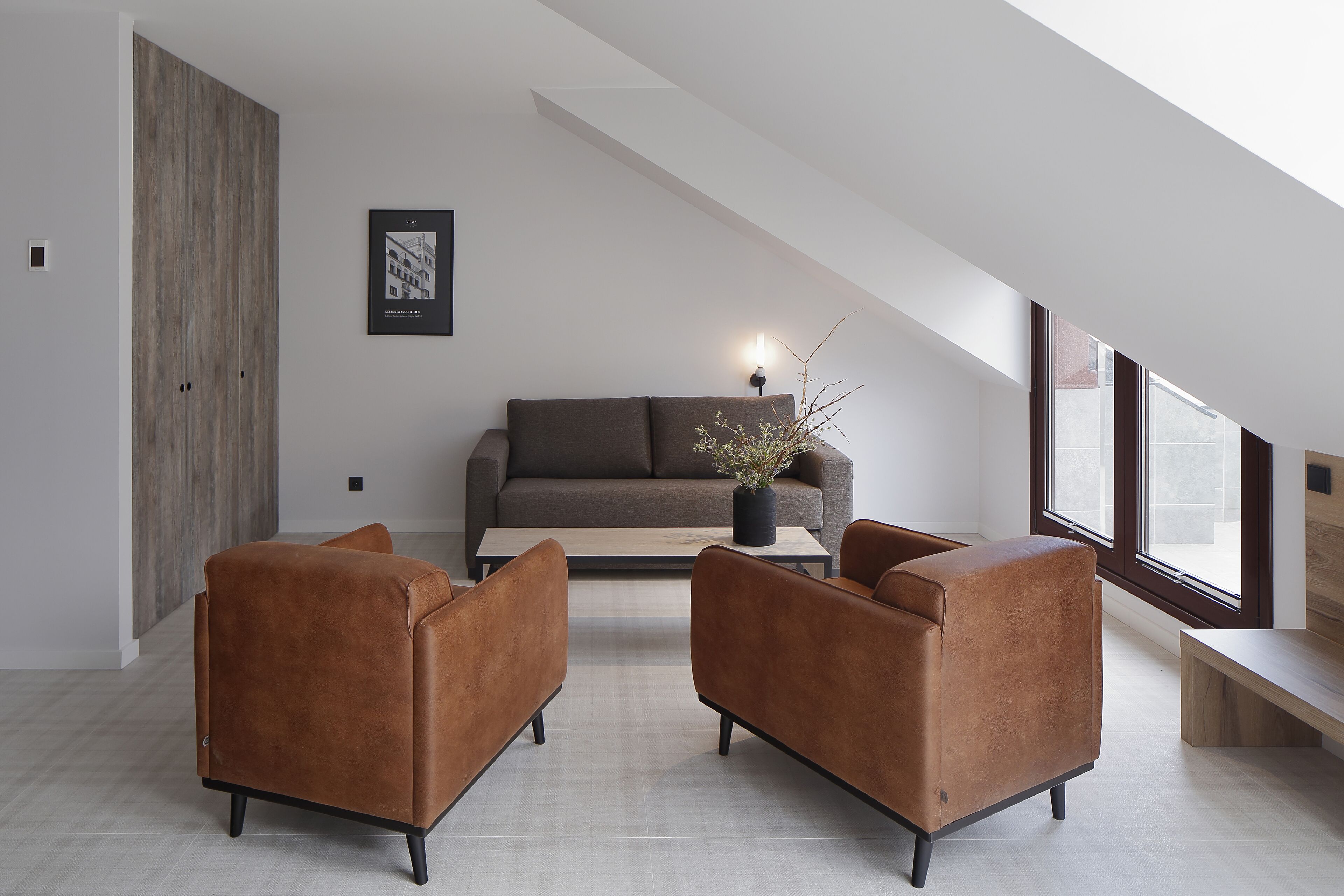 Un salon moderne avec un plafond de style industriel, un canapé gris, des fauteuils en cuir marron et une table basse.
