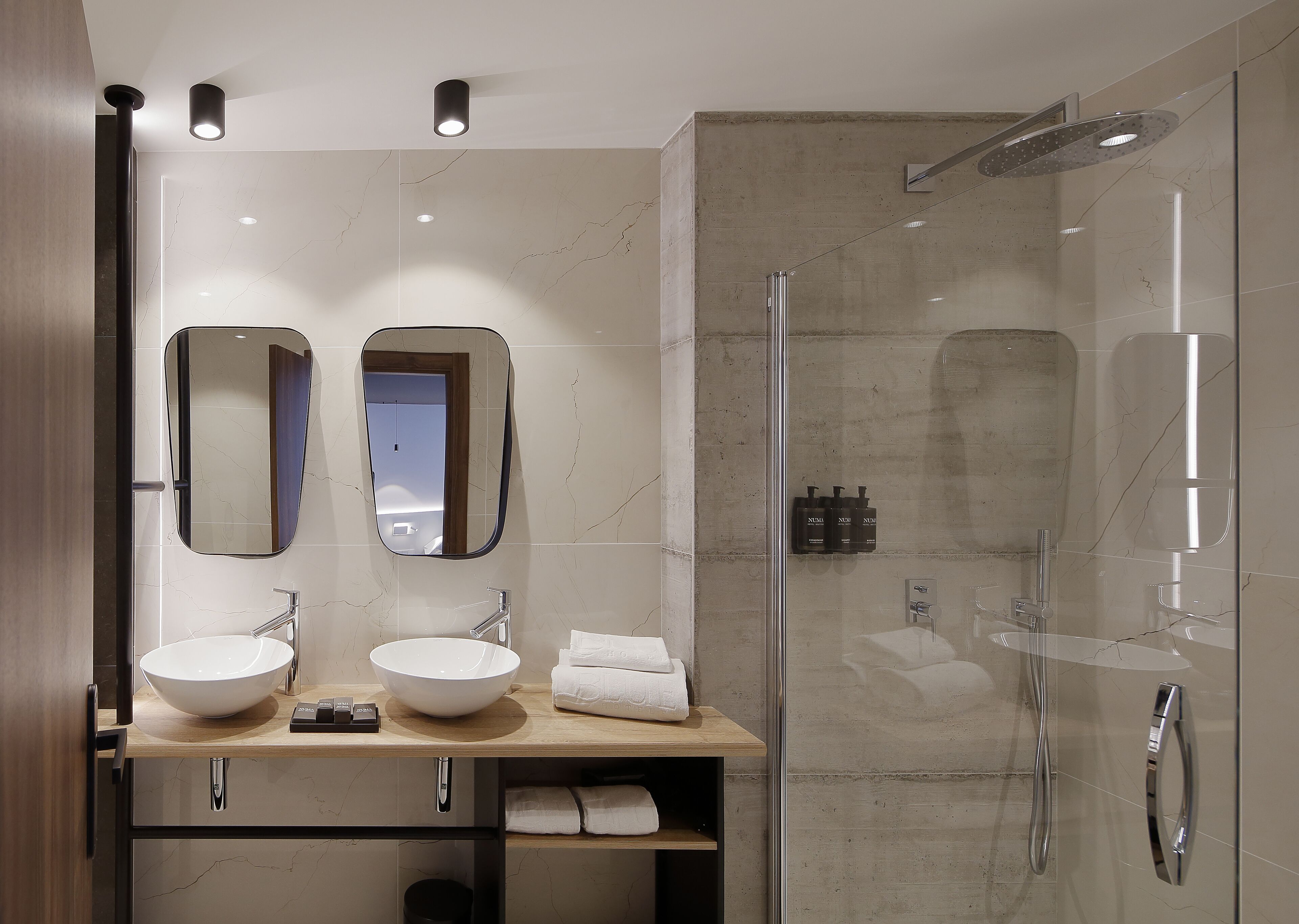 A modern bathroom with two sinks, a large mirror, and a glass-enclosed shower.