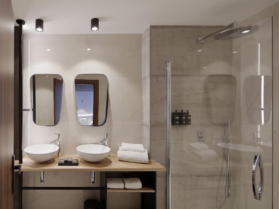 A modern bathroom with two sinks, a large mirror, and a glass-enclosed shower.